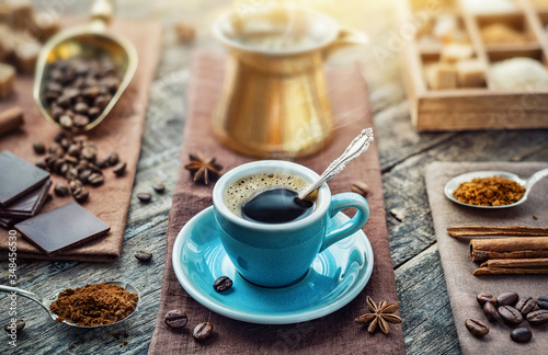 A cup of aromatic black coffee, a coffee maker, coffee beans of different varieties on the table. Morning espresso or Americano coffee for breakfast in a beautiful brown cup. © Tryfonov