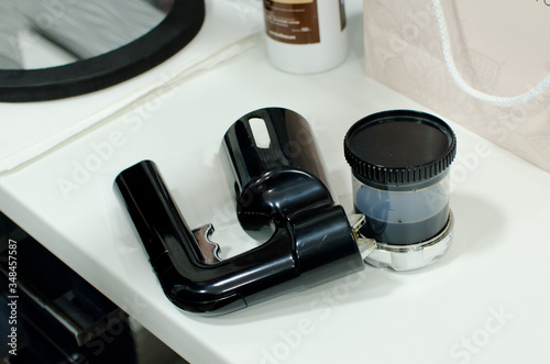 isolated airbrush pistol with plastic cup of paint  for instant tanning, tan spray body paint on white table in professional beauty salon