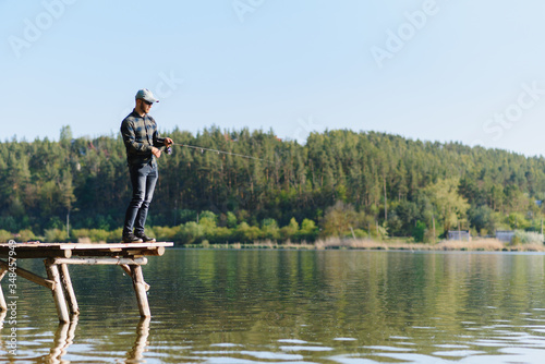 Fishing for pike, perch, carp. Fisherman with rod, spinning reel on river bank. Man catching fish, pulling rod while fishing on lake, pond with text space. Wild nature. The concept of rural getaway.