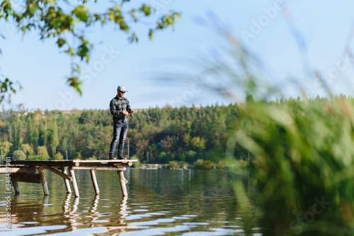 Fishing in river.A fisherman with a fishing rod on the river bank. Man fisherman catches a fish pike.Fishing, spinning reel, fish, Breg rivers. - The concept of a rural getaway. Article about fishing. © Serhii