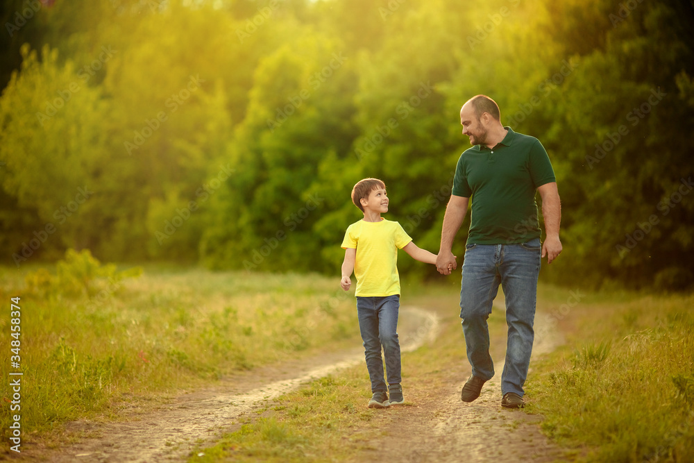 A happy family. father and son walk along the road and hold hands for a walk in the forest. A happy family. father and son walk along the road and hold hands for a walk in the forest.