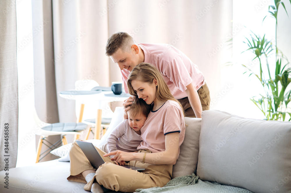Happy family time. Young dad and mom spend leisure time at home with their little beloved son, they are sitting on the couch and watching something interesting in the laptop Happy family time. Young dad and mom spend leisure time at home with their little beloved son, they are sitting on the couch and watching something interesting in the laptop