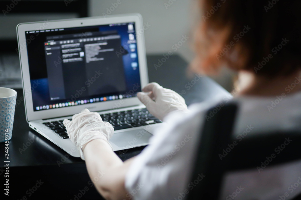 a woman works at home in a mask and gloves on a computer, remote work a woman works at home in a mask and gloves on a computer, remote work