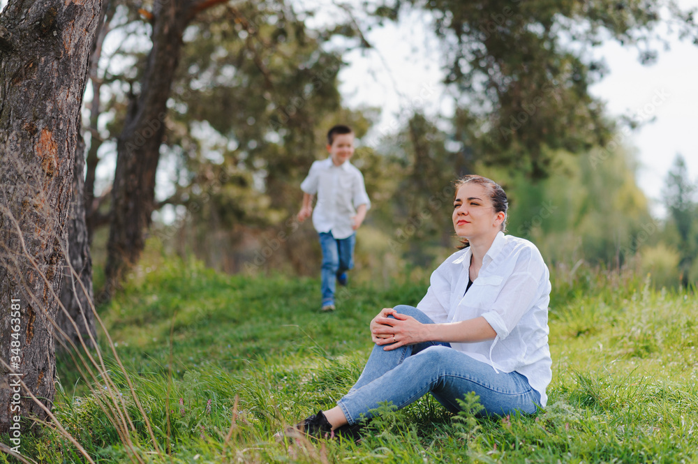 Fototapeta premium Happy young mother is playing with her baby in a park on a green lawn. Happiness and harmony of family life. Great family vacation. Good weekend. Mothers Day. Holiday. The concept of a happy family