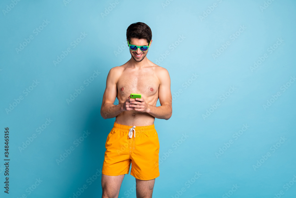 Photo of cheerful positive addicted man browsing through telephone while having relax at the ocean near empty space isolated pastel blue color background