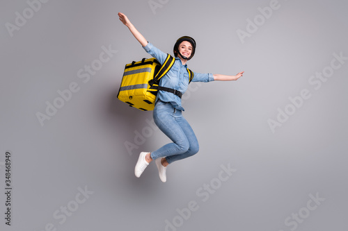 Full size photo of cheerful courier girl jump hold hands imagine she can fly deliver food quarantine covid-19 carry thermal backpack wear denim jeans shirt isolated gray color background