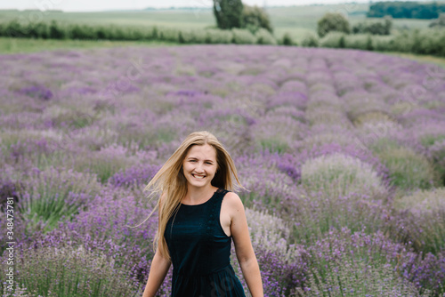 Fototapeta Naklejka Na Ścianę i Meble -  Beautiful woman walk and look on the lavender field on sunset in France. Beautiful girl in dress stand on purple the lavender field. Soft focus. Enjoy on the floral glade, summer nature.
