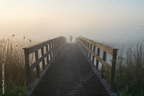 Cyclist on a wooden bridge over a river on a foggy morning in the dutch countryside.