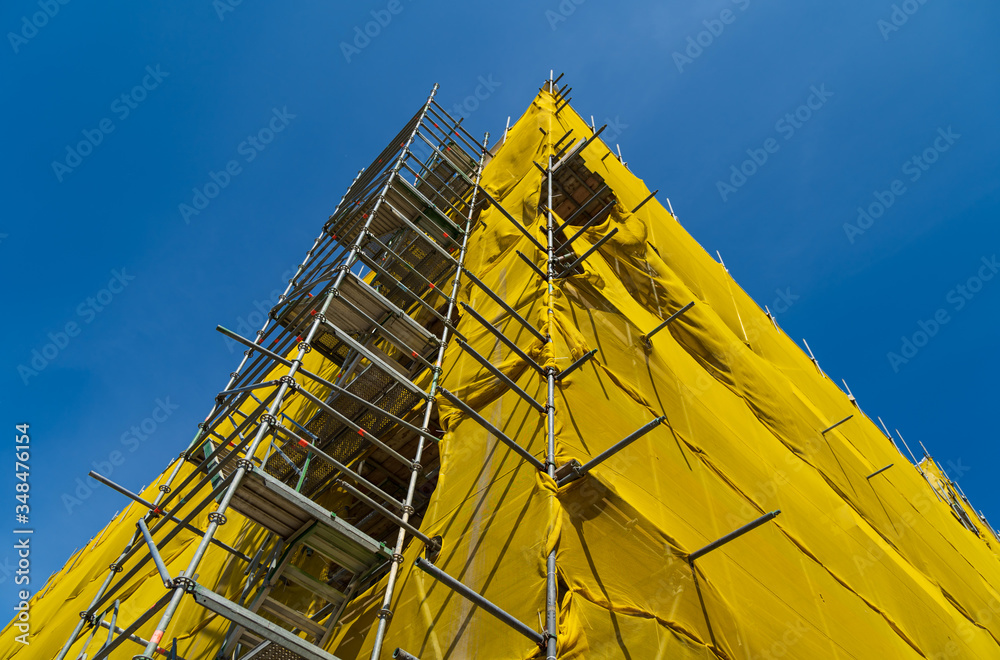 Fototapeta A constuction-site with a building in scaffolding and yellow mesh.