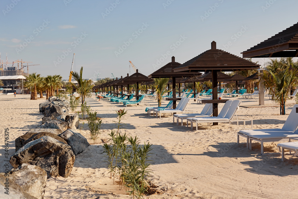 White sun loungers under brown wooden umbrellas stand on the beach. The concept of rest