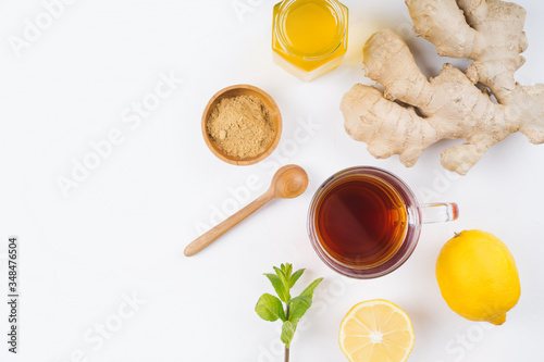 A glass cup of black natural tea with ginger  lemon  mint and honey isolated on wooden white rustic background. Healthy vitamin drink.