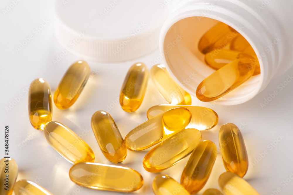Close-up on yellow capsules scattered from a bottle on white background Close-up on yellow capsules scattered from a bottle on white background