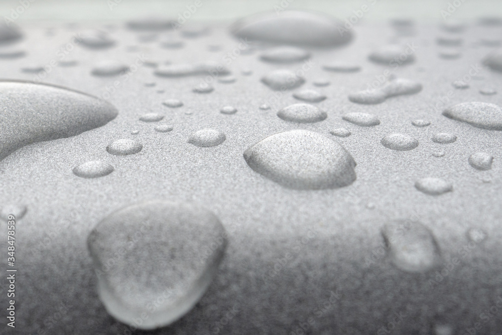 Transparent drops of water on a silver glossy metal surface. Abstract background with strong blur zone of blur Transparent drops of water on a silver glossy metal surface. Abstract background with strong blur zone of blur