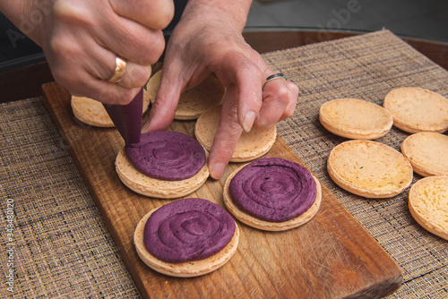 Cooking macarons cookies at home. Female hand squeezes cream on homemade cookie .on a wooden board