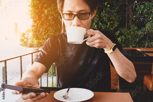 Lifestyle of young asian man whih his hand using or looking at his smartphone and drinking a coffee  in the cafe photo