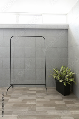 front view of empty black metal clothes drying rack or clothesline with stainless steel rail and plant in washing room