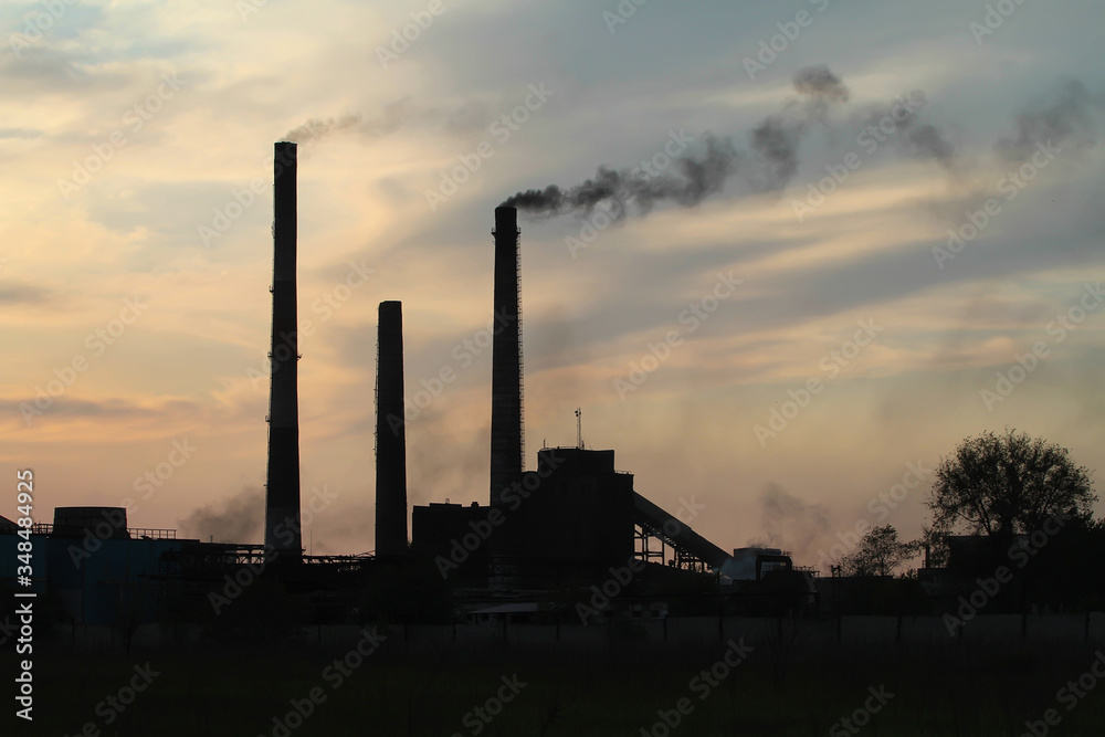Smoking chimneys of a plant against the setting sun