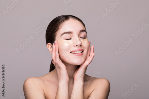 Young woman with an eye patches touching temples isolated on gray background. Cosmetics, skin stress concept