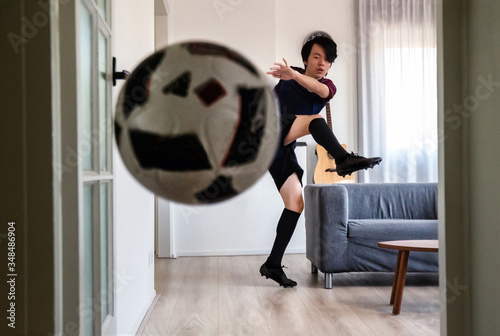 Young Asian boy kicking ball at home during home quarantine ( home activity during COVID-19 pandemic lockdown )