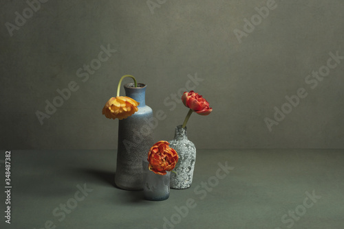 Three vintage vases with red and orange peony tulips in grey room.