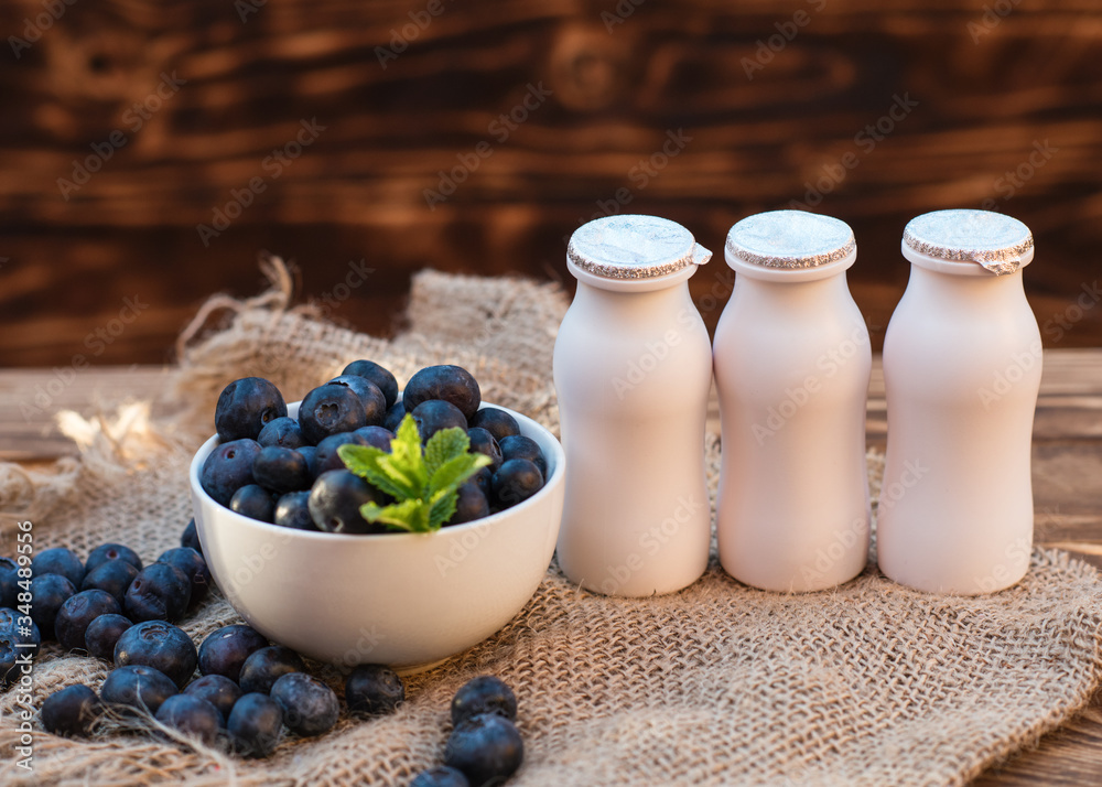 Fresh summer blueberry with leaf in the white bowl, yogurt bottles on the brown wooden background Fresh summer blueberry with leaf in the white bowl, yogurt bottles on the brown wooden background