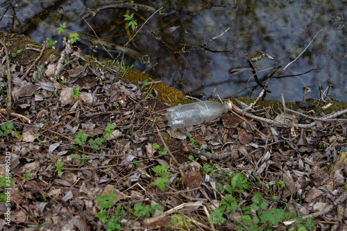 A dirty plastic bottle lies on the shore. Pollution of a dirty river. Pollution of the environment.