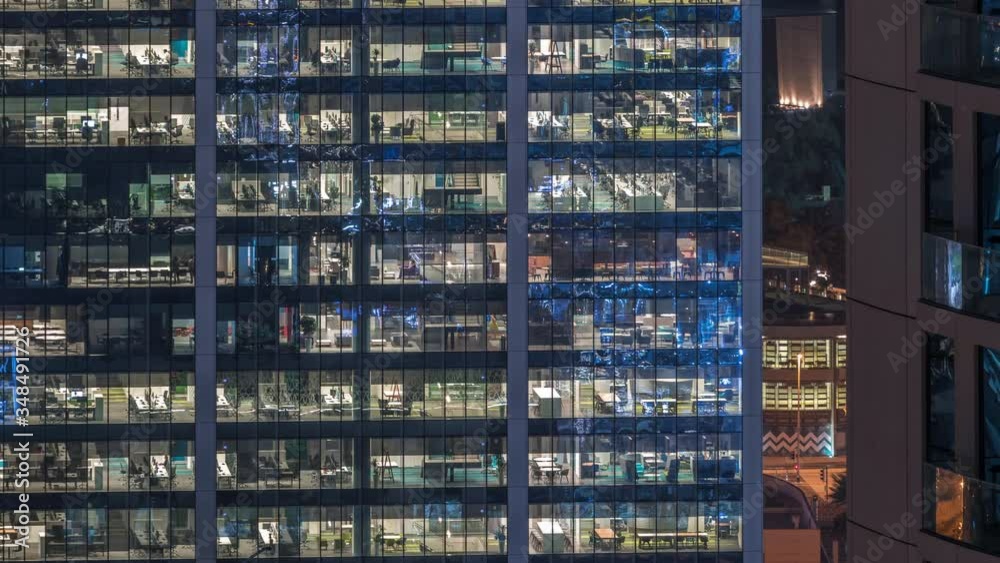 Office building exterior during late evening with interior lights on and people working inside skyscraper night timelapse. Aerial close up view from above with many illuminated windows. Office building exterior during late evening with interior lights on and people working inside skyscraper night timelapse. Aerial close up view from above with many illuminated windows.