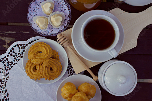 A cup of tea with butter biscuits and pastries, natural light on wooden table