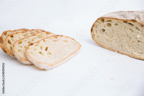 Cut freshly baked loaf of wheat bread and slices. Closeup shot. Isolated object on white background. Homemade food or breakfast concept