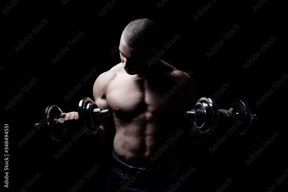 Attraktiver und muskulöser Mann posiert mit Hanteln vor schwarzem Hintergrund 