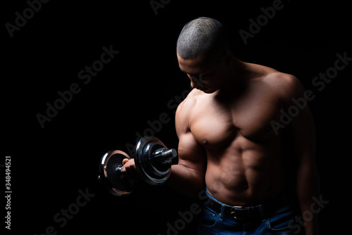 Attraktiver und muskulöser Mann posiert mit Hanteln vor schwarzem Hintergrund 
