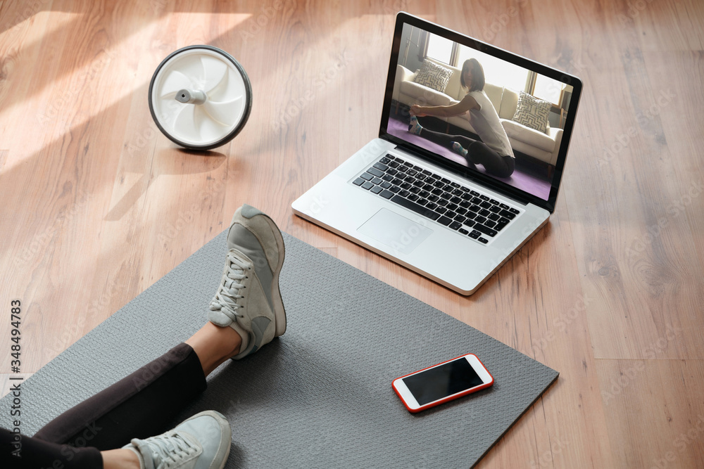 Closeup of young fit woman training indoors using laptop for watching yoga classes online. Home online workout. Home fitness during pandemic, quarantine and self isolation - obrazy, fototapety, plakaty 