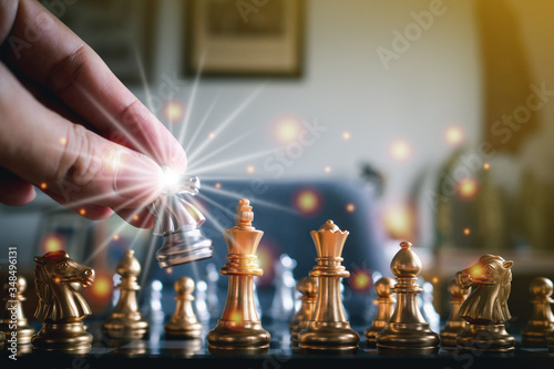 Close-up of hand holding a gold knight on chessboard with effect light. Business game competitive strategy. Concept of strategic for business.