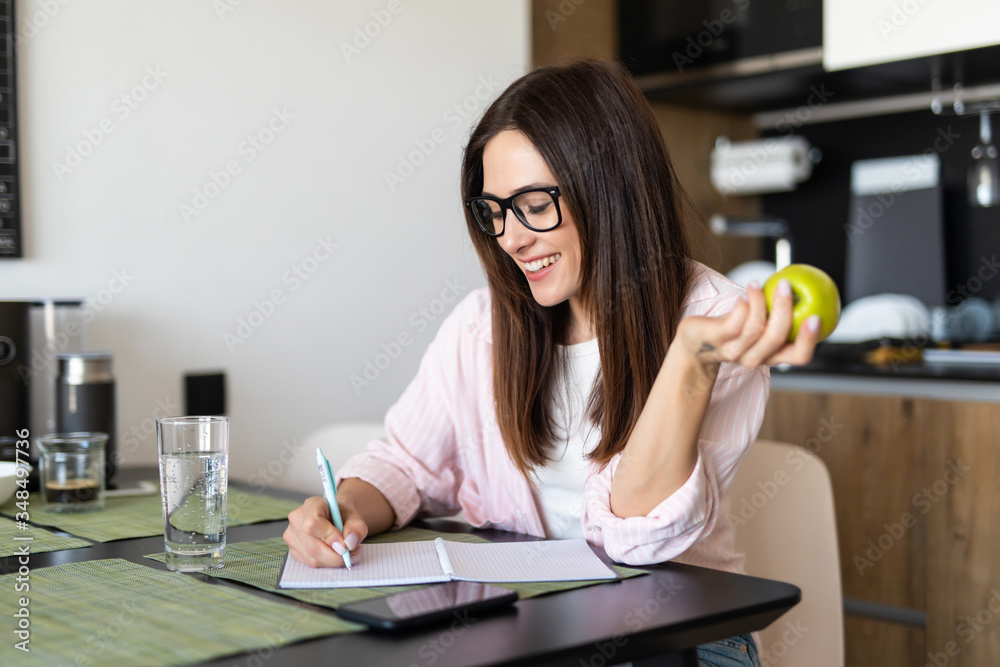 Healthy food concept. Young woman sitting at the table with apple and write on pad - obrazy, fototapety, plakaty 