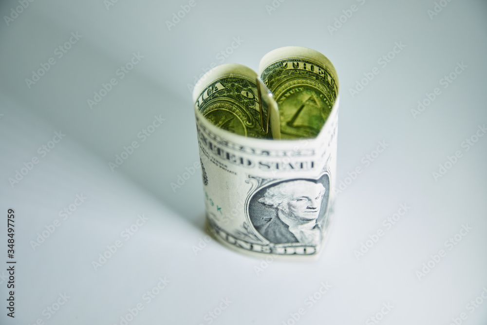 Heart folded from one dollar bill over gray background with copy space