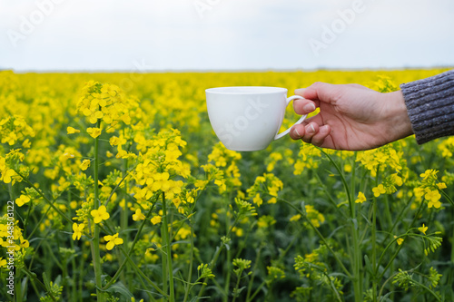 Female hand on a background of yellow flowers holding a cup of coffee. outdoors 