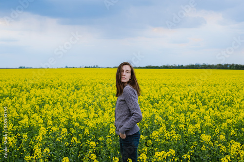 portrait of a girl standing among a field of yellow rapeseed flowers. 