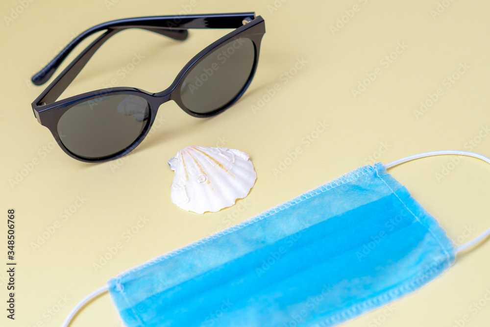 Closeup of sunglasses, medical face mask, seashell on a yellow background. Travel concept.
