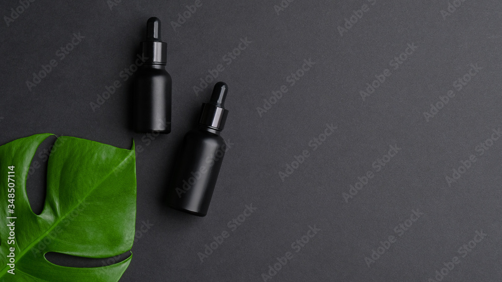 Black dropper bottles and tropical leaf on black background with copy space. Natural organic skin care product, luxury premium packaging design mockup - obrazy, fototapety, plakaty 