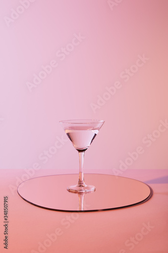 cocktail glass with liquid on mirror with reflection on pink background