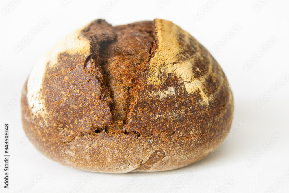 Delicious rye bread baked at home. Crispy round dark loaf isolated on white background. Studio shot. Selective focus. Side view. Homemade bakery and cooking at home concept