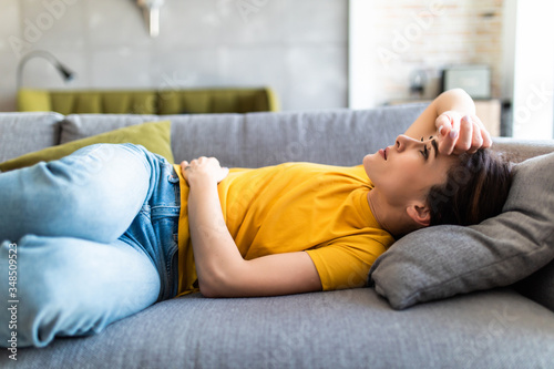 Tableau sur toile Sick woman lying on sofa in the living room with stomach ache
