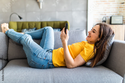 Smiling beautiful girl using mobile phone relaxing on a couch at home