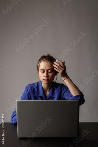 Young woman in blue with glass of water using a laptop.