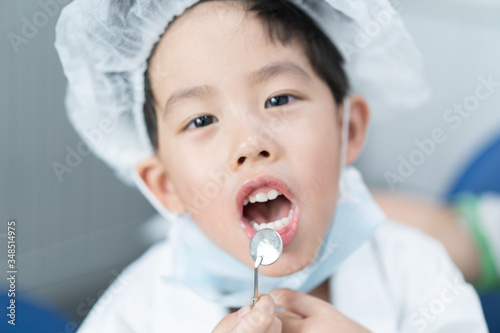 Little Asian dentist boy with a dentist suit try to check his patient teeth: Future career and career dream concept.
