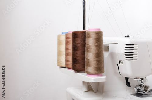 Closeup of spool of beige threads and professional overlock macnine against white background photo