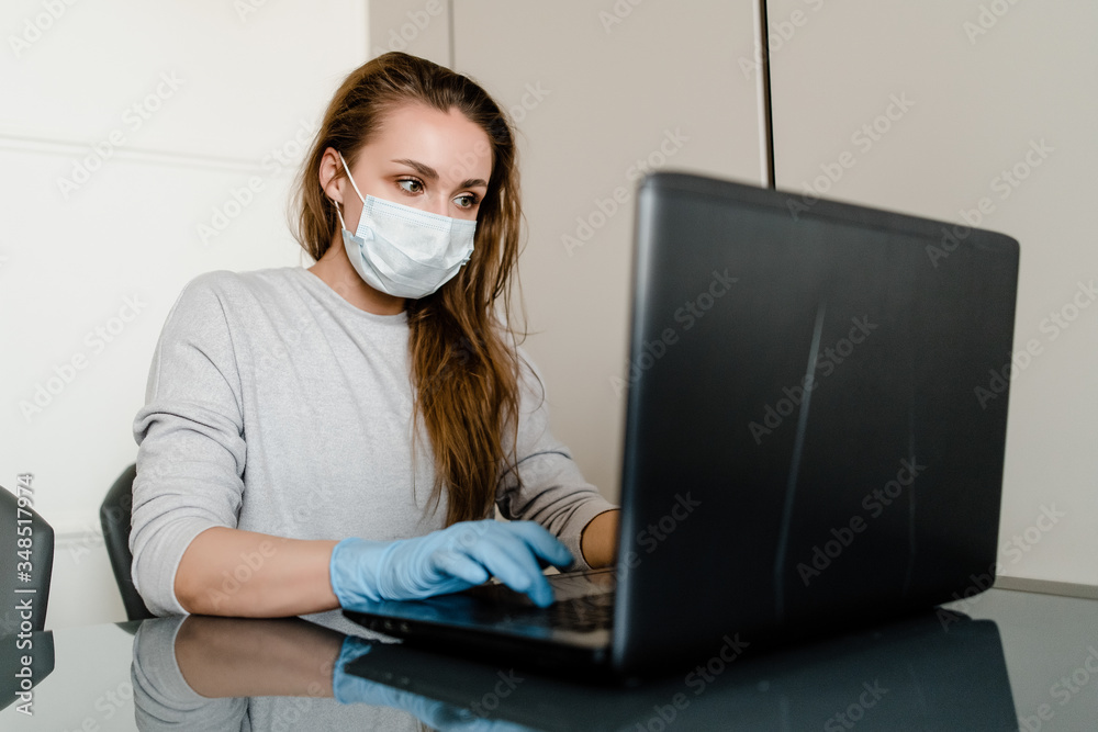 woman working on laptop from home office wearing mask and gloves