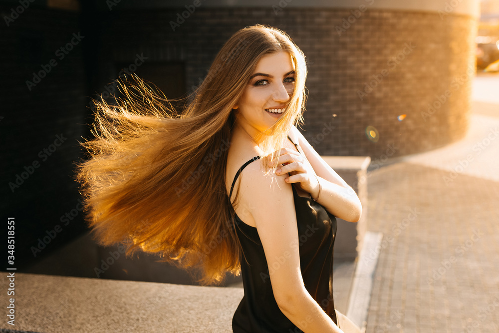 Obraz premium Smiling business woman in black dress sitting. Summer. isolated woman portrait with healthy developing hair. Woman at sunset looks at the camera.