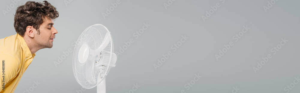 Man in front of electric fan isolated on grey, panoramic shot - obrazy, fototapety, plakaty 