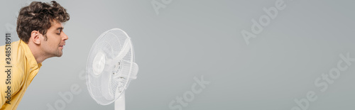 Man in front of electric fan isolated on grey, panoramic shot